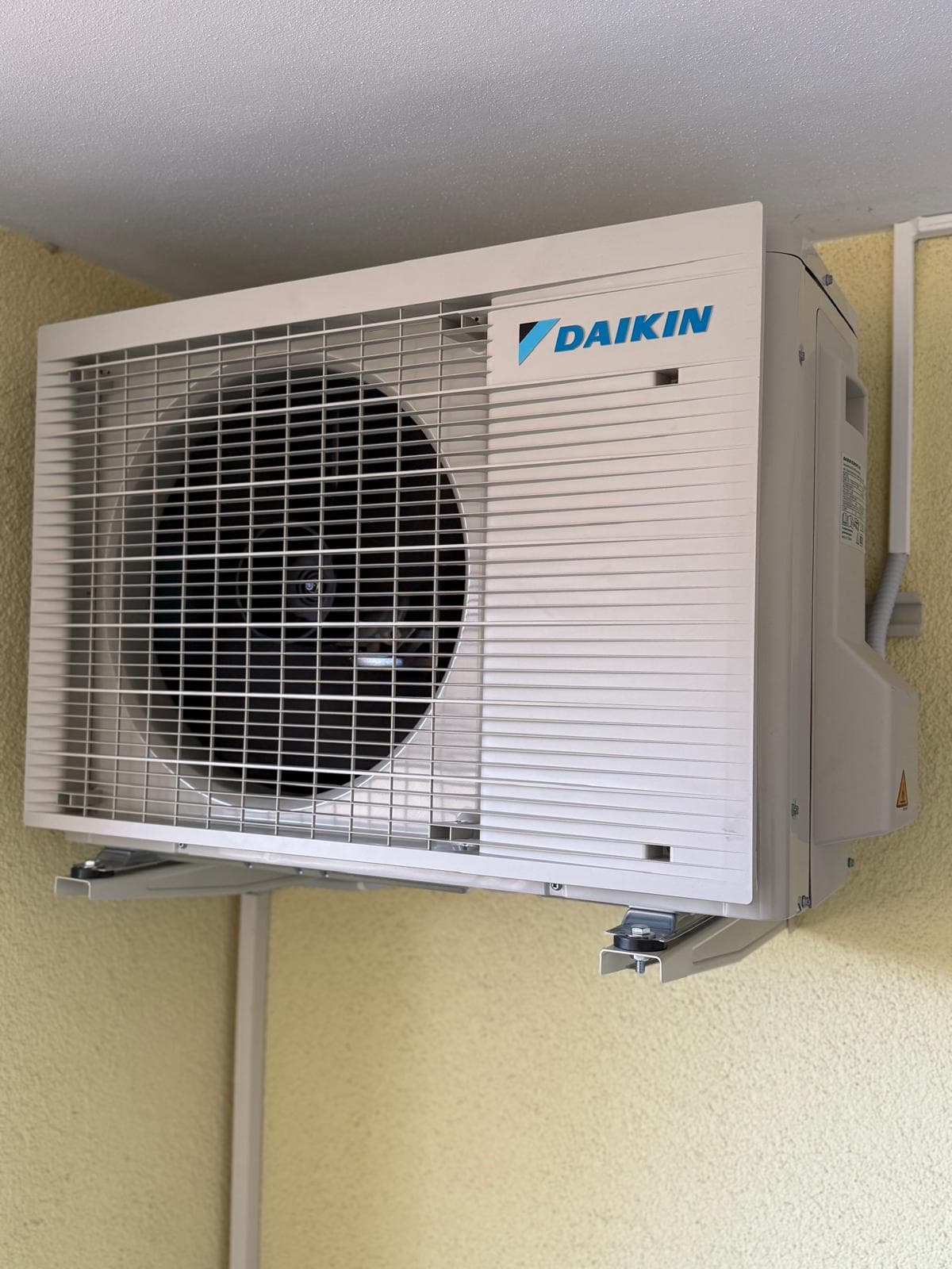 Daikin Außeneinheit mit Metallkonsolen an der Wand befestigt, geschützt unter einem Vordach