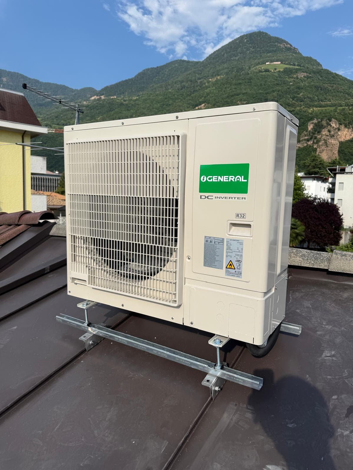General DC Inverter R32 Außeneinheit auf Metallschienen, auf einem Flachdach mit Bergen im Hintergrund