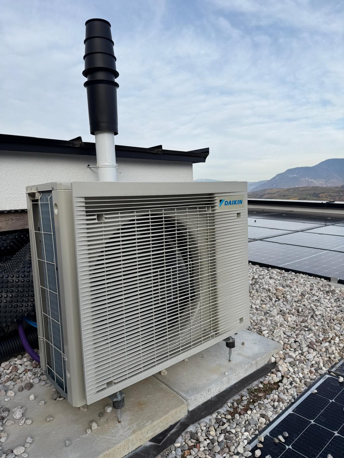 Daikin Außeneinheit auf einem Betonsockel, auf einem Flachdach neben Photovoltaikmodulen